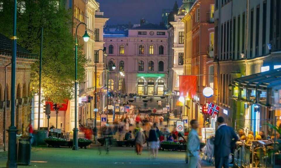 Karl Johans gate er Oslos hovedgate, fylt med butikker, restauranter og utesteder som sørger for liv og røre hele dagen, utover kvelden og inn i natten. (Foto: Colourbox.com) Folk i Karl Johan en kveld med gatelys, skilt og flagg.