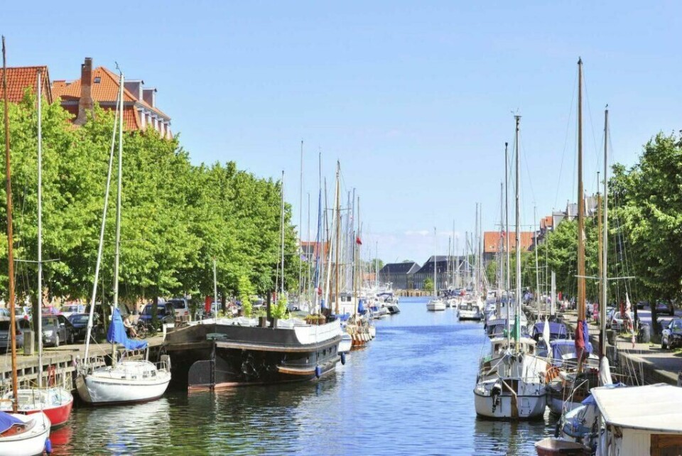 Er det deilig å være Norsk i Danmark. Det synes hverfall vi! (Foto: Apollo) Bildet viser en idyllisk kanal omgitt av grønne trær og båter som ligger til kai. Kanalens speilblanke vann reflekterer mastene på seilbåtene, og langs kanalbredden er det murhus med røde tak. Himmelen er klar og blå, og atmosfæren virker rolig og sommerlig.