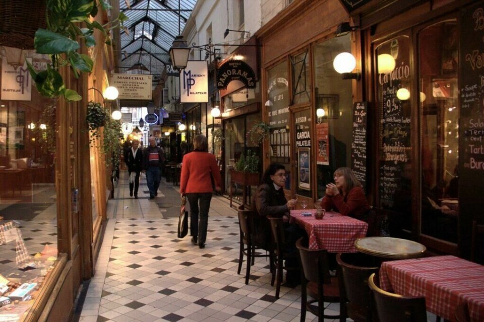 Passage des Panoramas ble bygget i 1799 og er den første overbygde gangveien i Paris. (Foto: Nicolas Vigier via Wikimedia Commons) Bilde fra innsiden av Passage des Panoramas i Paris som er byens eldste overbygde gangveier, her ser du en dame som går midt i mens det er en koselig atmosfære fra klassiske butikker samt bord med stoler som tilhører en kafe. Eiffeltårnet, Triumfbuen, Louvre, Champs-Élysées og Notre Dame er alle severdigheter de fleste av oss allerede assosierer med Paris. Byen som også kalles «kjærlighetens by» kan by på mye mer en de klassiske turistfellene (som absolutt burde oppleves!), og vi har derfor samlet ti skjulte skatter du finner i Paris.