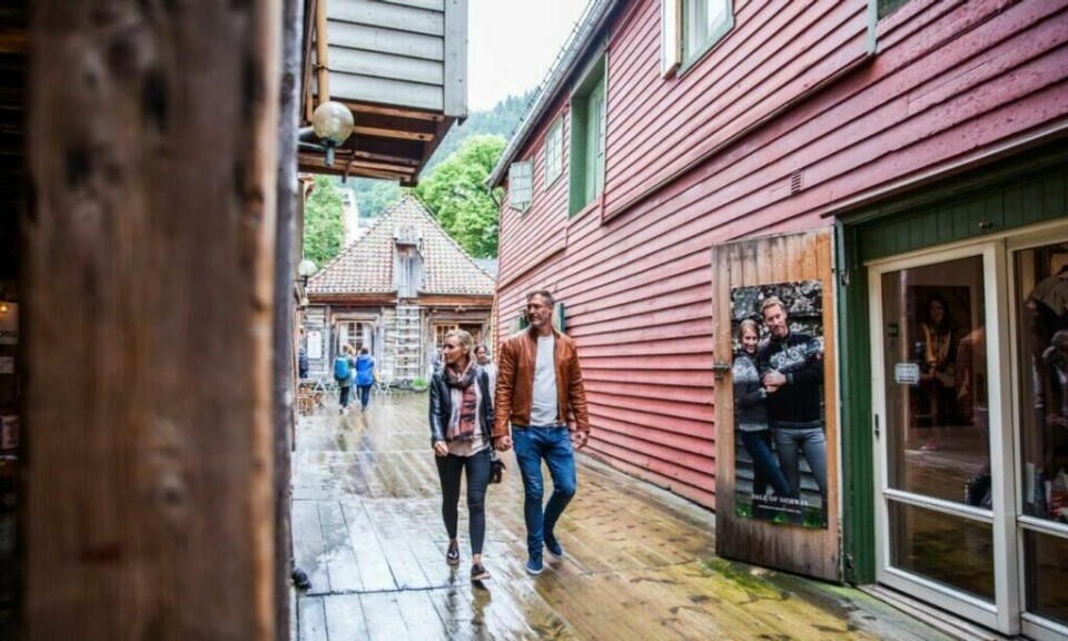 Skjult bak den ikoniske fasaden på Bryggen ligger en hemmelig verden av passasjer, småbutikker, gallerier og studioer. (Foto: Martin Håndlykken / Visit Norway) Bilde av par i smug på bryggen i Bergen.