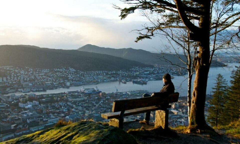 Fløyfjellet eller Fløyen er en av Bergens mest populære turistattraksjoner. (Foto: Øyvind Heen / Visit Norway) Person som sitter på en benk på toppen av Fløyfjellet, med spektakulær utsikt.