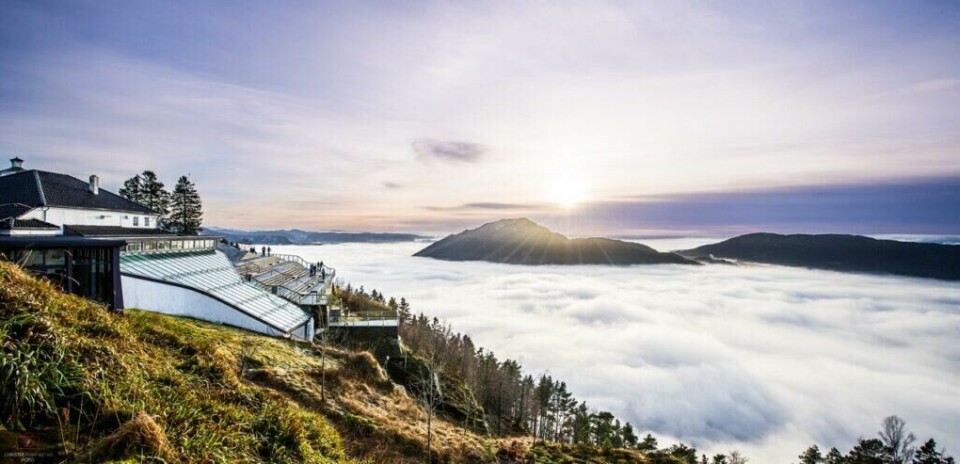 Fløyen: På toppen av Fløyfjellet med utsikt over tåkehav og fjelltopper. (Foto: Visit Bergen / Christer Rønnestad - visitBergen.com) På toppen av Fløyfjellet, over skyene, med utsikt til glassbygg og fjell.