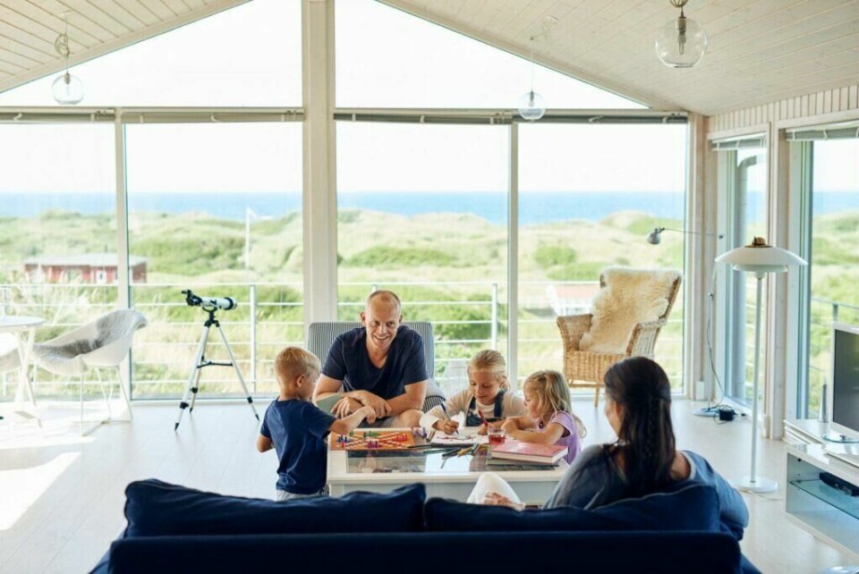 Et feriehus i Danmark passer ekstra bra for familieferien, da man får tid til å være mye sammen, samtidig som alle kan gjøre som de har lyst ti. (Foto: Niclas Jessen / VisitDenmark) mann og kone med te små barn som er inne på en hytte i danmark nær sjøen. tegner og leker utsikt mot sjøen