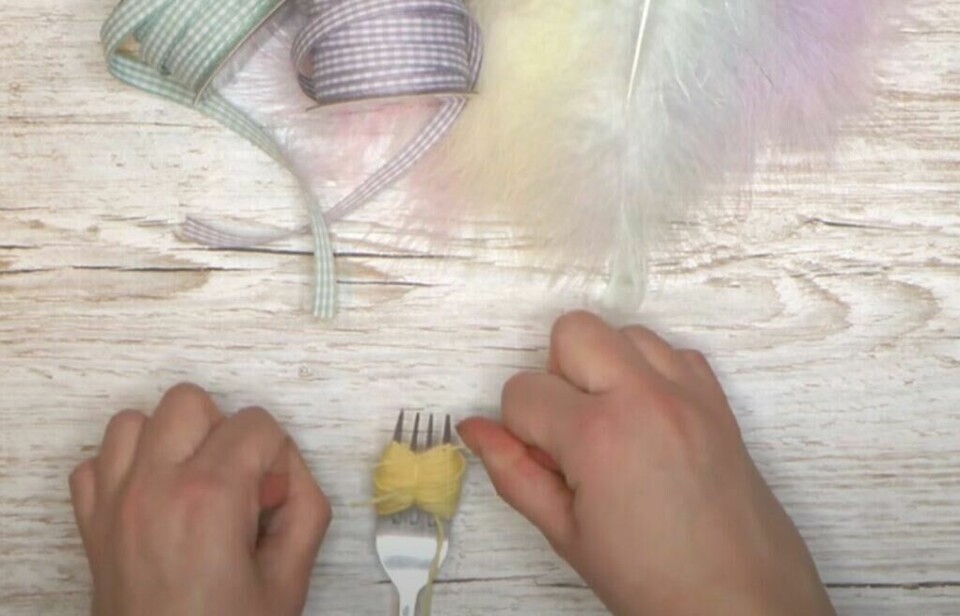 Bruk den første løse tråden til å binde sammen dusken du har laget, men husk å ikke klippe av de lange trådene! (Foto: Kreativeideer.no) Fingre som binder sammen dusk til påskekylling med gult garn.