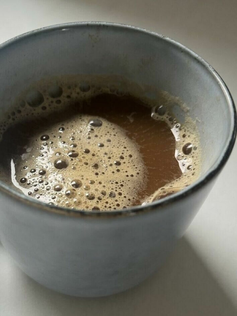 Mellom klokken 8 og 9 får vi alle en forhøyning i kortisolnivå og dette har innvirkning på når du bør drikke dagens første koppe med kaffe. Vi forklarer. Bilde av en blå keramikk-kopp med sort kaffe på marmorbord. Vi forteller om overraskende forskning som tilsier at det ikke er lurt å drikke kaffe om morgenen og hvorfor!