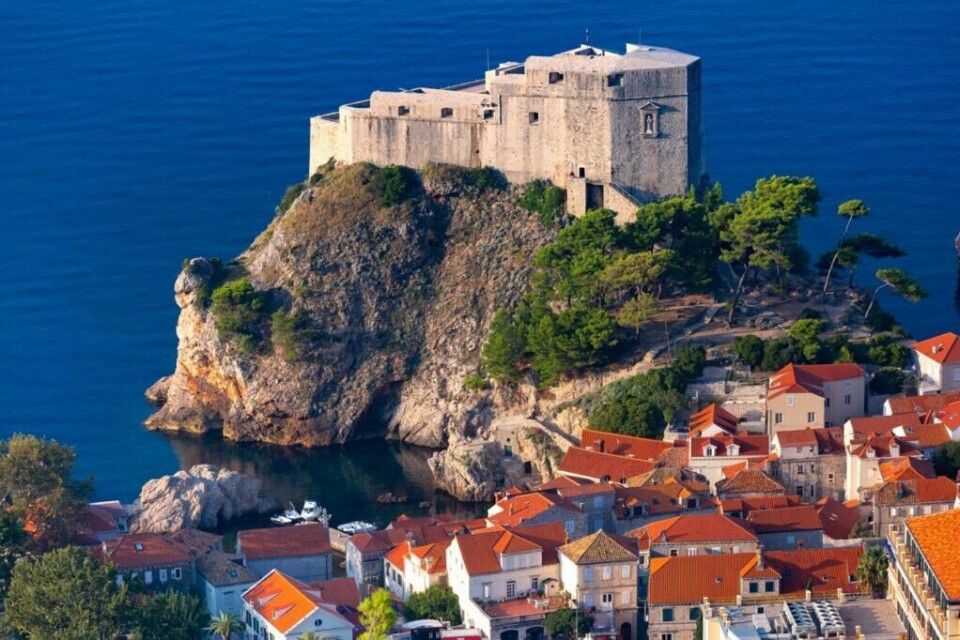 Fort Lovrijenac er et vakkert skue i Dubrovnik, og er absolutt verdt å få med seg når man besøker den populære byen i Kroatia. (Foto: Colourbox) Bilde av Fort Lovrijenac (Dubrovnik, Kroatia) i bakgrunnen som står på en klippe med blått hav rundt. I forgrunnen ser man klassiske murhus med rødt tak. Dubrovnik byr på alt fra vakre strender til historiske severdigheter som Fort Lovrijenac, som også har blitt brukt som sett i den populære serien Game of Thrones.