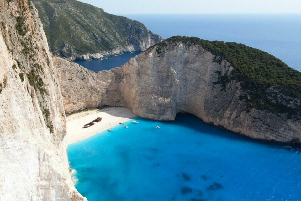 Øyhopping i Hellas: Navagio-stranden på Zakynthos er kanskje en av de mest velkjente strendene i Hellas. (Foto: Colourbox) Bilde av Navagio-stranden på Zakynthos i Hellas. Her ser du en kritthvit strand med et båtvrak som er omringet av bratte klipper og knallblått hav. Her får du en utfyllende guide på øyhopping i Hellas hvor vi gir deg tre reiseruter, pakkeliste og gode tips til hvordan man gjør øyhopping med barn. Opplev plasser som Santorini, Kreta, Athen, Paros, Naxos, Korfu og Mykonos.