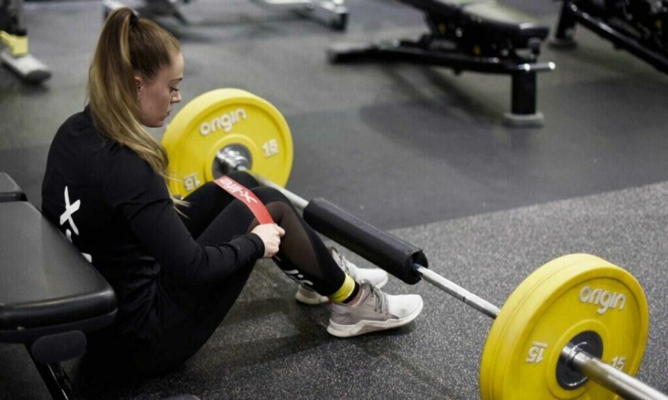 Treningen hjemme ka ´n gjennomføres minst like effektivt som på treningssenter med et godt treningsprogram og riktig utstyr. (Foto: @coacholsen) Bilde av jente på gulv på trenigssenter som trener med strikk og gule vekter.