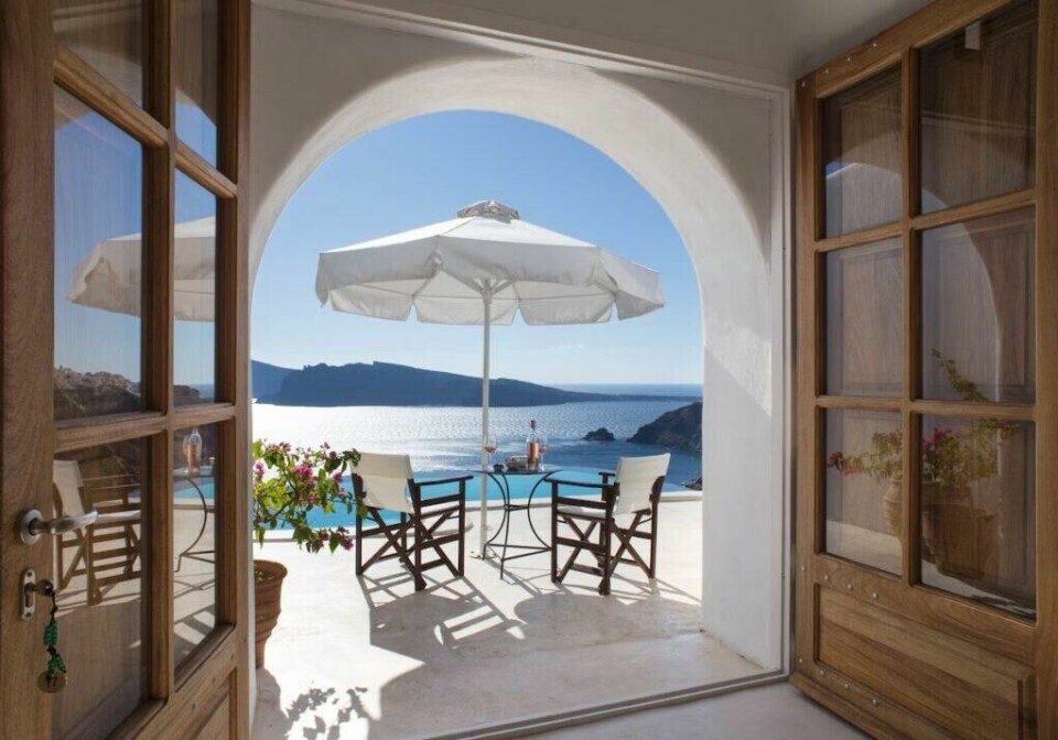 Perivolas er kåret til det beste hotellet på Santorini i Hellas av det velkjente reisemagasinet Condé Nast Traveller. (Foto: Hotels.com) Bilde tatt fra innsiden av Perivolas-hotellet på Santorini. Gjennom den buede døren kan man se to stoler og et bord med parasoll som er vitne til en flott utsikt over havet. Vi har skrevet om fem ting man bør se og gjøre på Santorini i Hellas, samt avslører hvilket hotell på Santorini som er kåret til det beste. Her finner du også restplasser til Santorini og billige reiser til de greske øya