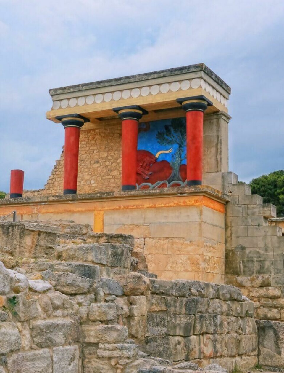 Palasset i Knossos er et imponerende arkeologisk sted på Kreta i Hellas, og er perfekt for deg som elsker historie. Bilde av ruiner i Knossos på Kreta i Hellas. Fargene på ruinene er enda tydelige med røde søyler og blå fresker. Vi har funnet restplasser til Kreta slik at du kan nyte billig reise til Hellas. Vi gir deg også fem tips til ting du må se og gjøre på den vakre øya, blant annet: Knossos, Samariaravinen, Elafonissi, Rethymnon og Spinalonga.