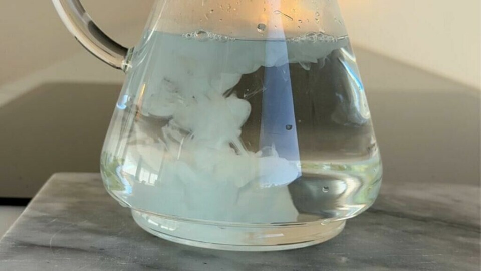 Oppskriften består av kun tre ingredienser – glansemiddel, eddik og vann – og gir en effektiv og miljøvennlig rengjøringsspray. (Foto: Kreative Ideer) Et glasskanne fylt med vann, hvor glansemiddel og eddik tilsettes og danner en skyete virvel i væsken – første steg i oppskriften på den virale rengjøringssprayen.