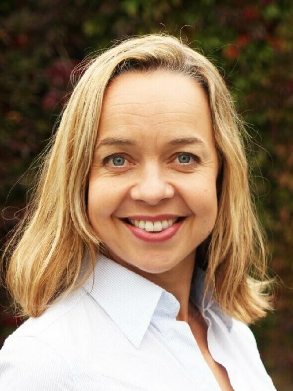 Paula Berstad er seniorforsker ved Kreftregisteret, Folkehelseinstituttet, Avdeling for tarmscreening. (Foto: FHI) Bildet viser en kvinne (Paula Berstad) med blondt hår og blå øyne, kledd i en lyseblå skjorte. Hun smiler varmt og ser rett mot kameraet. Bakgrunnen er en murvegg dekket av klatreplanter med høstfarger i rød- og grønntoner, som gir et levende og behagelig bakteppe. Bildets uttrykk er profesjonelt og vennlig, og egner seg godt til for eksempel et portrettintervju eller en faglig presentasjon.Paula Berstad er seniorforsker ved Kreftregisteret, Folkehelseinstituttet, Avdeling for tarmscreening.