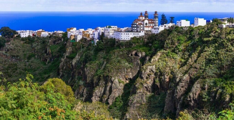 Vi har funnet frem billigere pakkereise-restplasser til den vakre Kanariøyen, og røper i samme slengen hvilken strand, restaurant og hotell som er besøkendes favoritt! (Foto: Colourbox) Bilde av landsby i frodige åser på Gran Canaria. Her ser du majestetiske fjell, grønne trær og busker og rosa blomster. Vi ahr funnet frem forslag til billige pakkereiser som du får billig med restplasser til den populære Kanariøyen med besøksfavoritter som Puerto Rico, Las Palmas og Playa del Inglés.