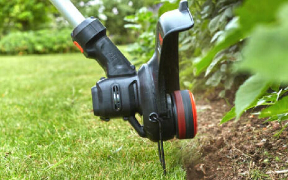 Gresstrimmere kommer med både tråd og blader. Tråd er mer effektivt på små områder, mens blader lettere tar grovere gress. (Foto: Garden Store) Nærbilde av kantklipper/ gresstrimmer som klipper gress i overgang mot bed i hage.