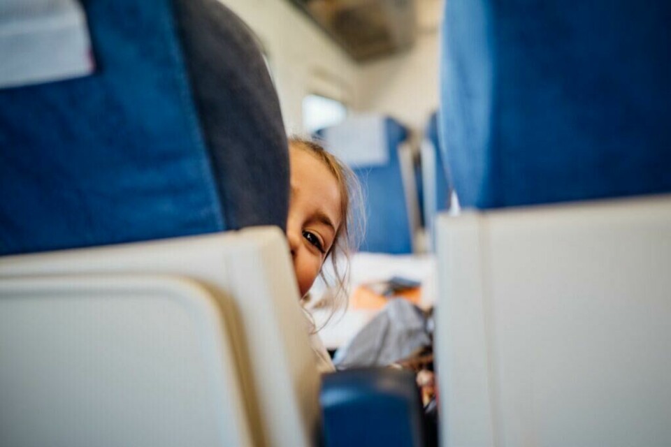 Barn som skriker/gråter eller ikke oppfører seg er nummer seks på listen over ting man irriteer seg over på flyturen. Dette tror kommunikasjonssjef i TUI, Anne Mørk-Løwengreen, skyldes det at det er lett å ha empati i en slik situasjon. (Foto: eldar nurkovic / Shutterstock / NTB) Et barn kikker nysgjerrig fram mellom setene på et fly, med bare halve ansiktet synlig og et lekent blikk i øyekroken. De blå seteryggene og nedslåtte bordene i forgrunnen gir tydelig inntrykk av et offentlig transportmiddel. Bildet fanger et klassisk og gjenkjennelig øyeblikk fra en reise, der barns nysgjerrighet og utforskertrang møter de voksnes behov for ro – et lite glimt av hverdagsdrama og søt forstyrrelse på farten.